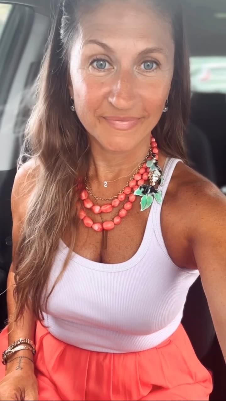 Margaret smiling in a car, wearing a white tank top and a coral beaded necklace
