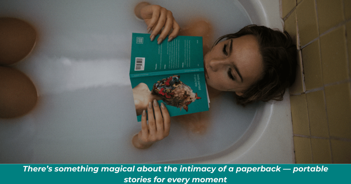 A woman in a bathtub reading a paperback book.