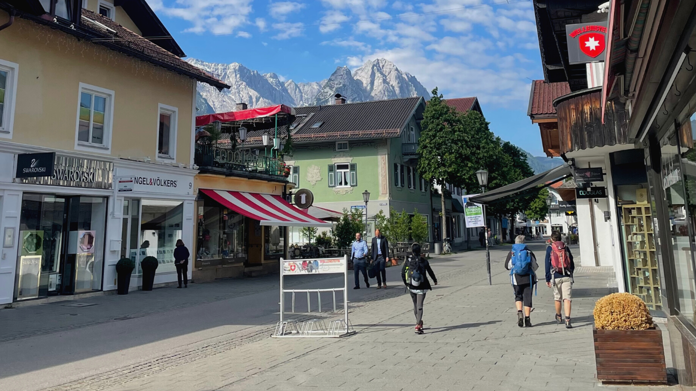 pedestrian street in Garmisch, Germany with traditional buildings and snow capped mountains in the background.