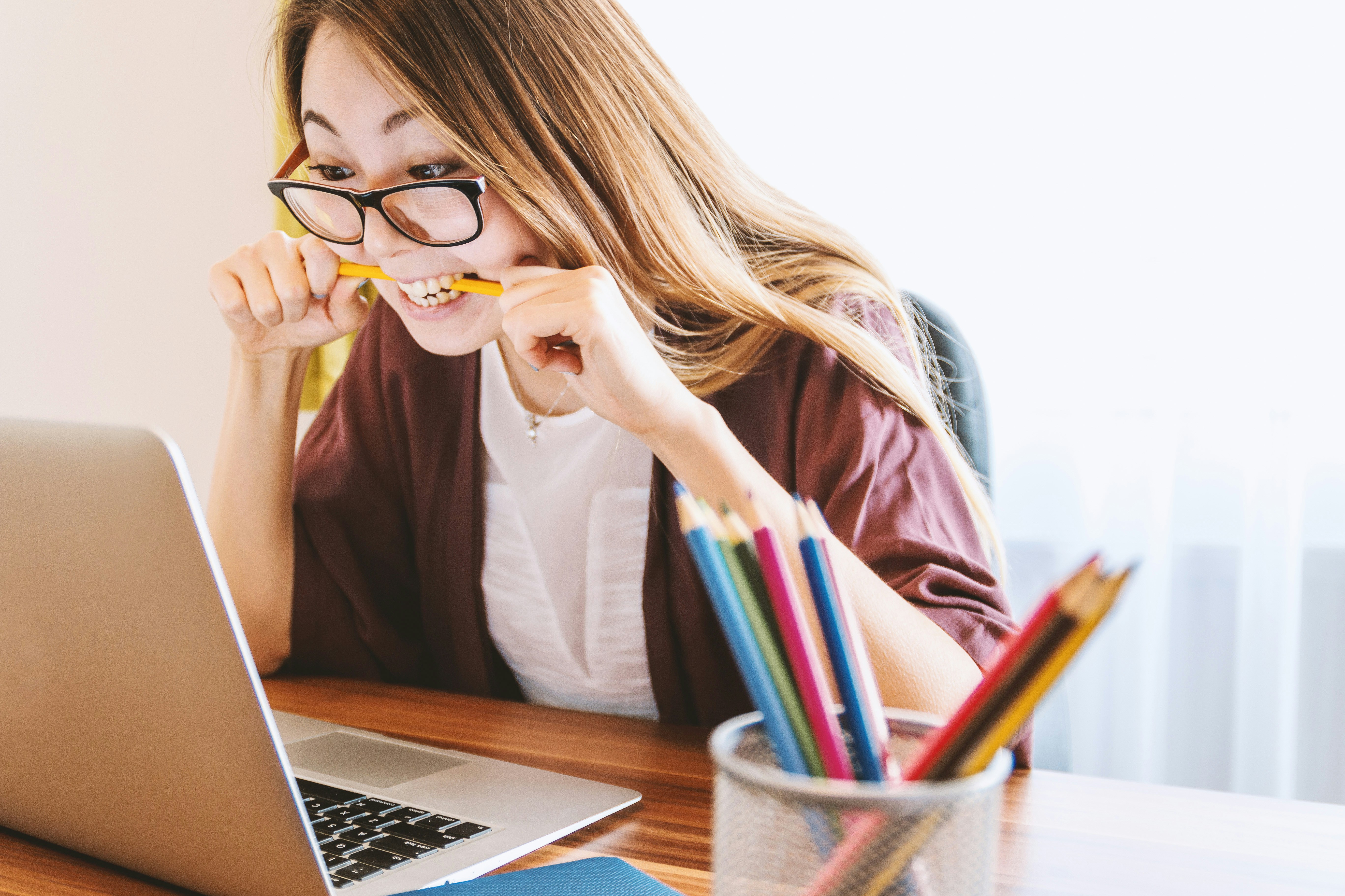 woman-biting-pencil-while-sitting-on-chair-in-front-of-computer-during-daytime