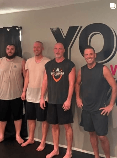 Group of men smiling after a workout in front of “YOU” wall inside the studio