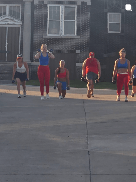 Group performing walking lunges outside in front of a brick building during a fitness bootcamp