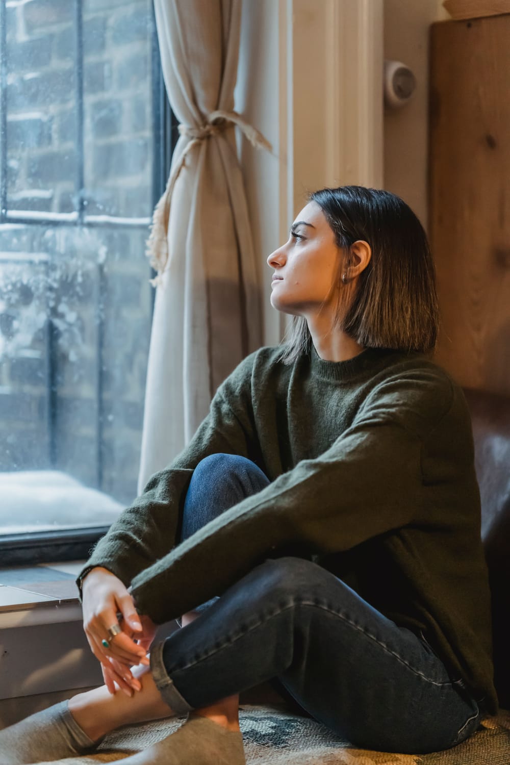 Une femme pensive assise près d’une fenêtre