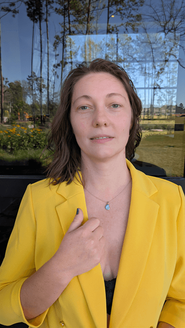 Anna Bohuslavska, inner guide for conscious moms, in a yellow blazer with her hand on her heart, standing in front of a glass wall