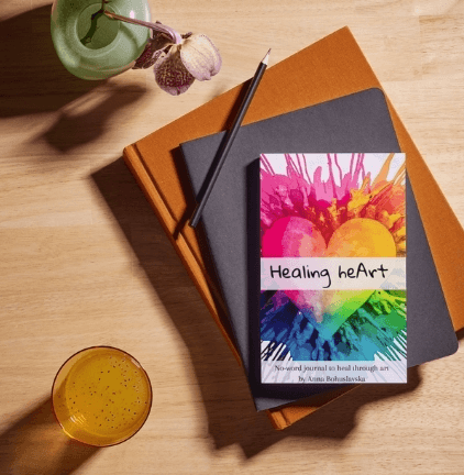 Cover of Healing HeArt by Anna Bohuslavska, a colorful heart painted in rainbow colors, resting on a stack of notebooks