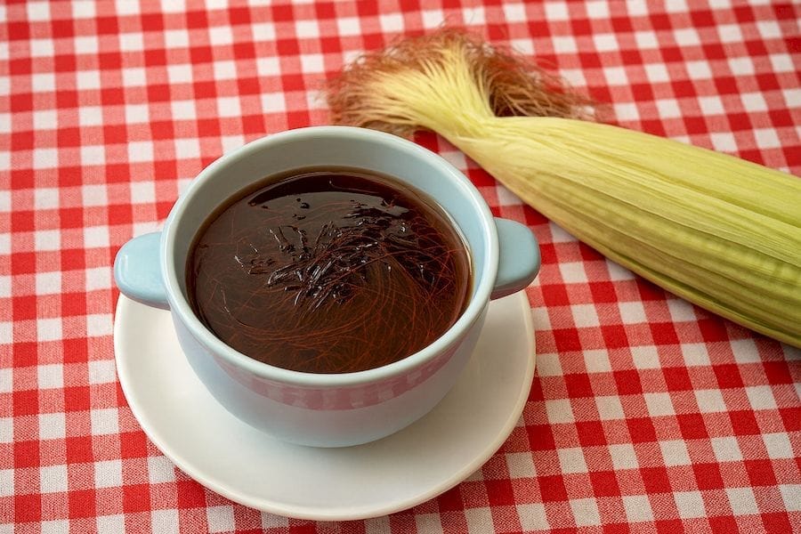 Vizelt hajtó, vesetámogató, kukoricabajusz tea egy világos kék csészében. Mellette egy cső kukorica kukoricabajusszal.
