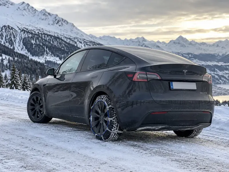 Tesla Model Y dans la neige avec chaînes illustrées sur une roue arrière
