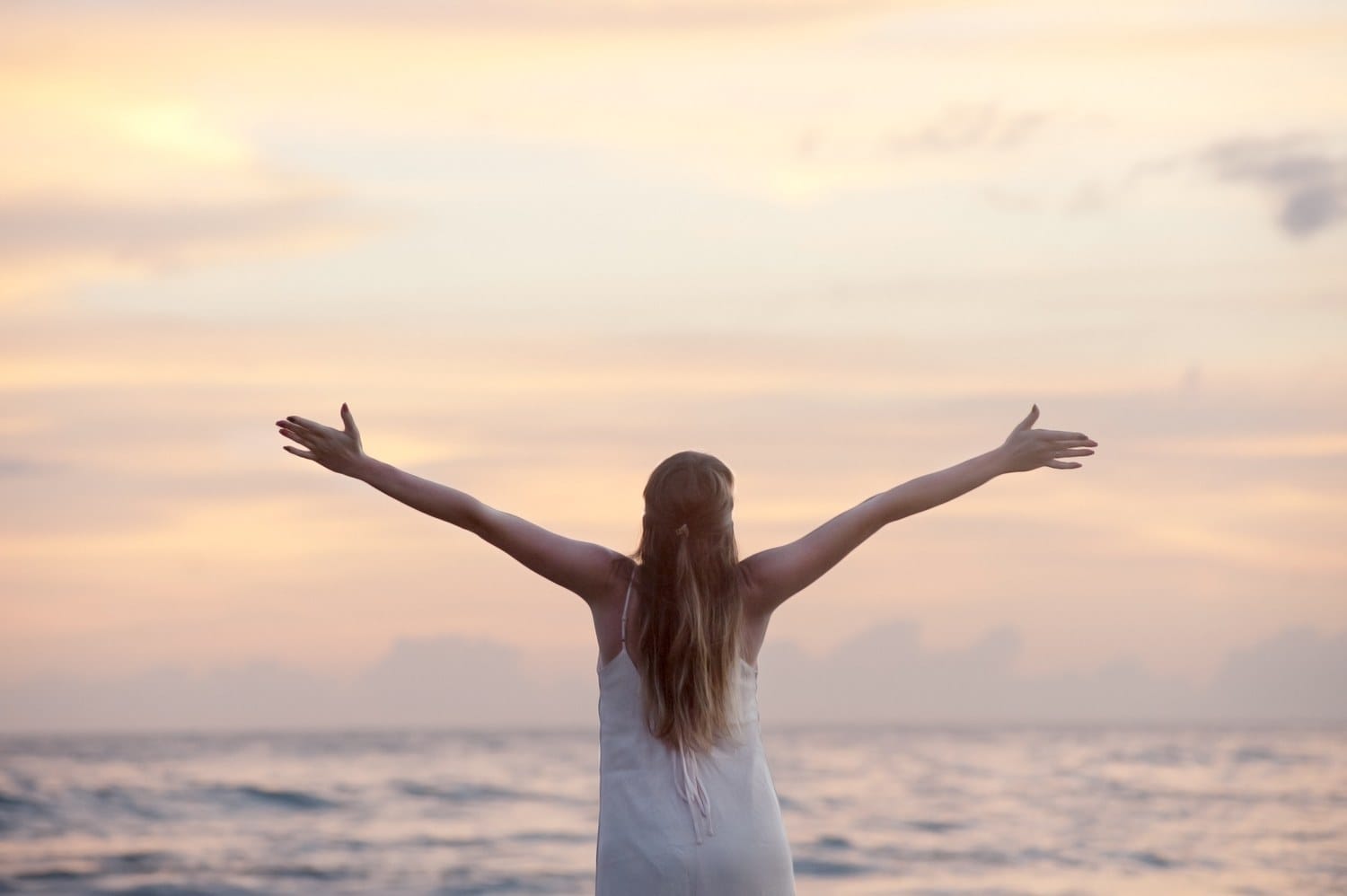 A woman with arms outstretched beside the water at sunrise