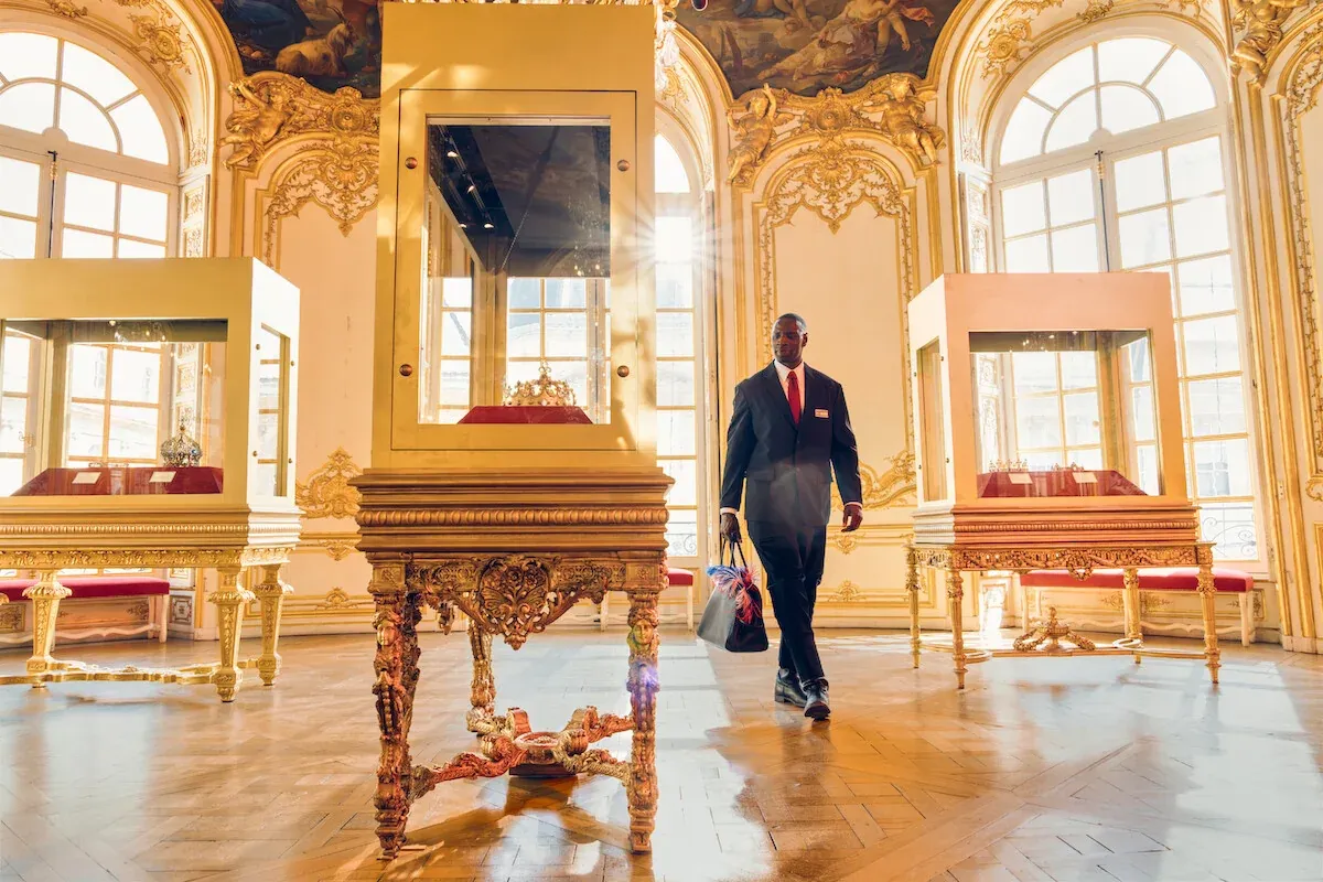 Omar Sy, travestito da custode, passa davanti alla teca della corona in una sala dorata in Lupin Parte 4