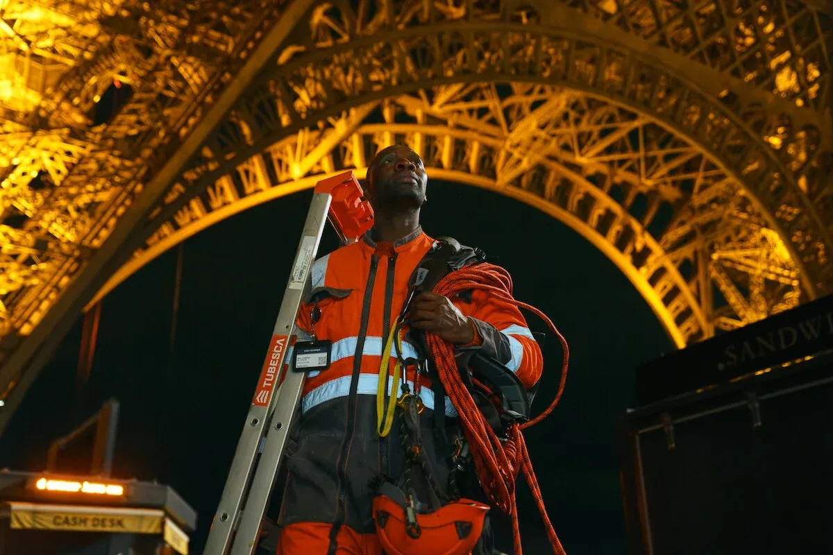 Omar Sy travestito da operaio con scala e corde sotto la Torre Eiffel di notte in Lupin Parte 4
