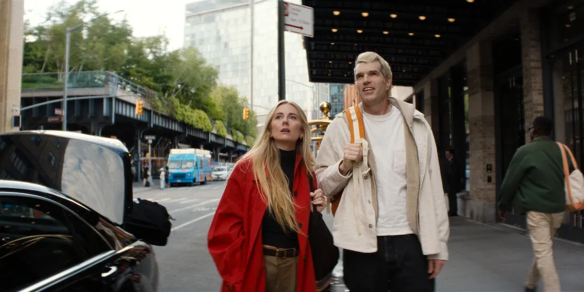 Morgan, con un cappotto rosso, e Sasha, con una giacca chiara e uno zaino in spalla, camminano su un marciapiede di New York in Nobody Wants This 3