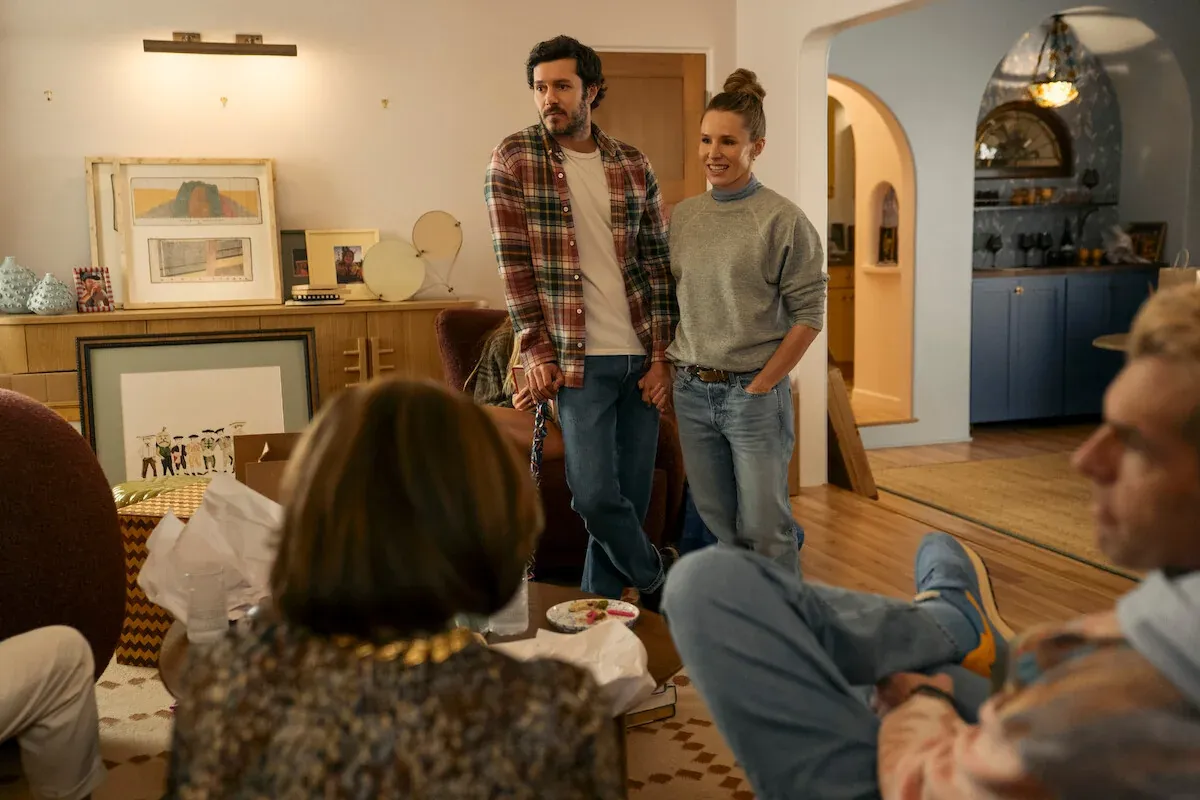 Noah, con una camicia a quadri, e Joanne, con una felpa grigia, si tengono per mano in piedi nel soggiorno di casa davanti ad alcune persone sedute, in Nobody Wants This 3