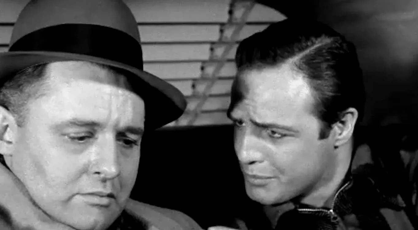 Charley, con il cappello, guarda in basso mentre Terry gli parla da vicino nel taxi, in Fronte del porto