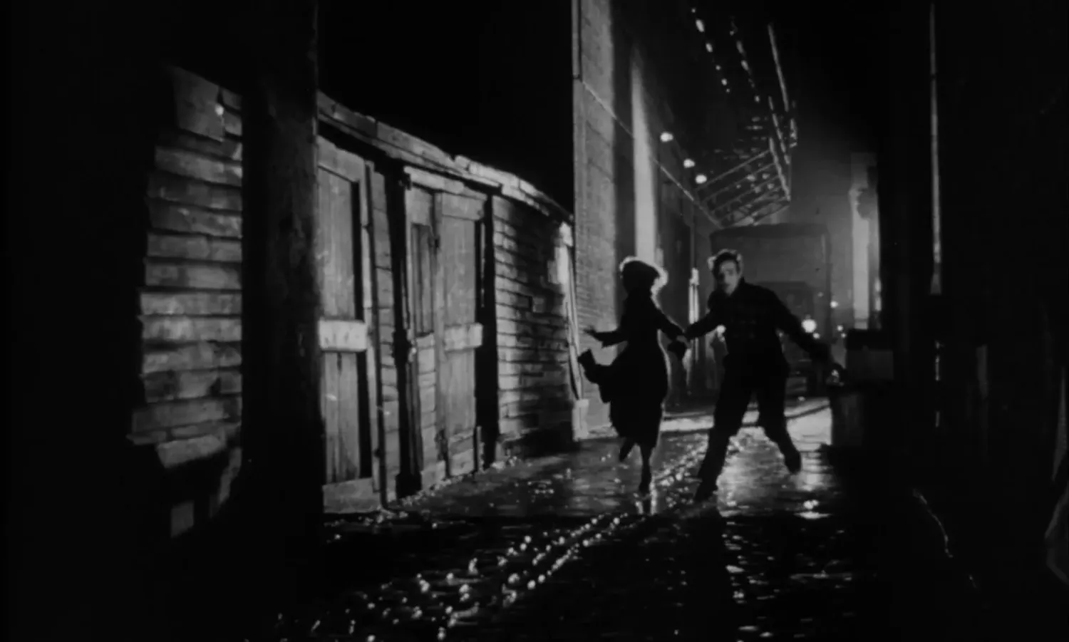 Terry ed Edie corrono tenendosi per mano in un vicolo bagnato, di notte, in Fronte del porto