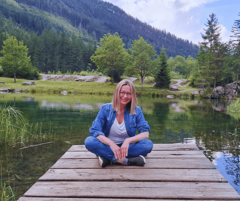 a woman sitting on the wooden pond on the lake with mountains behind her