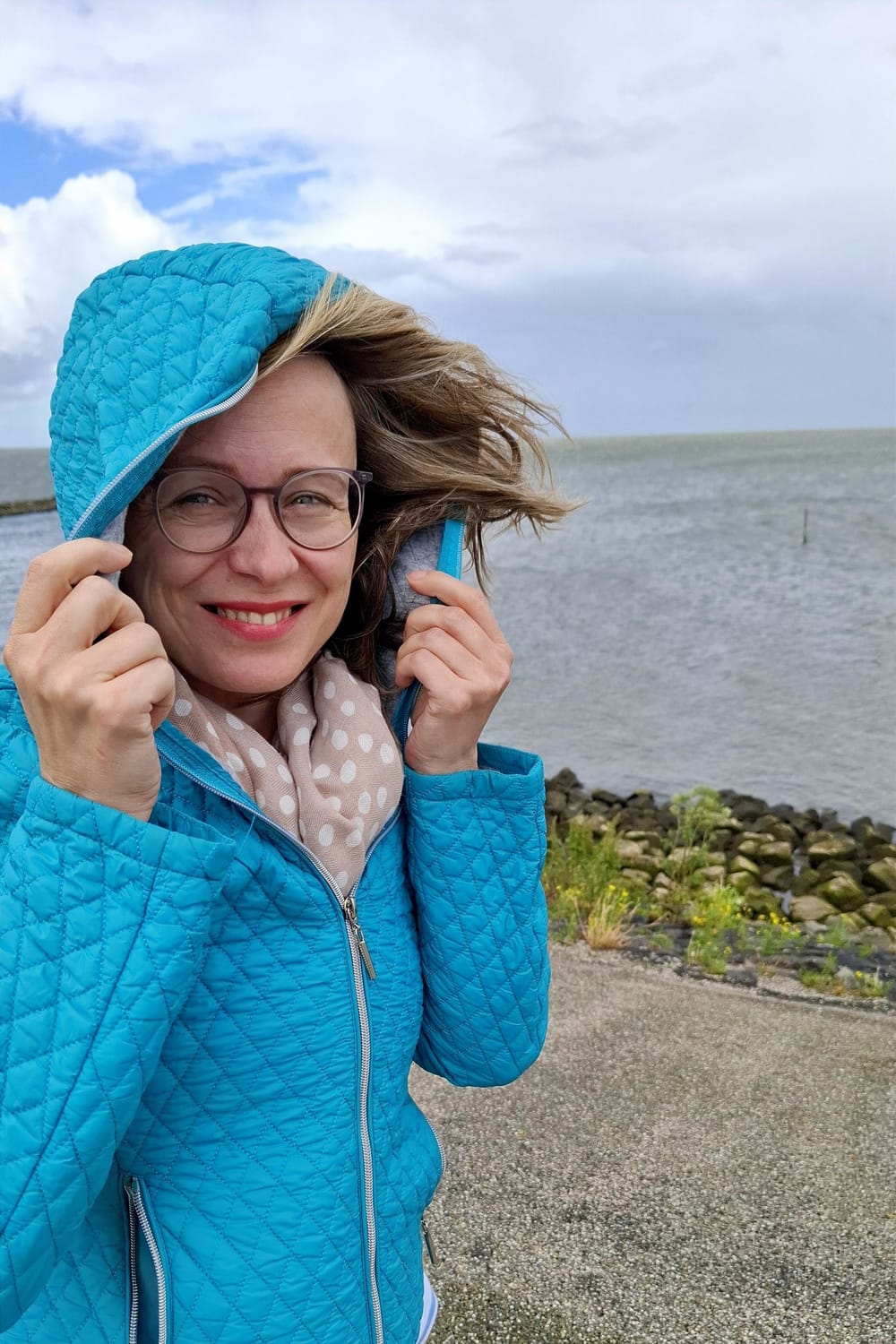a woman smiling and turning to the camera with ocean behind her