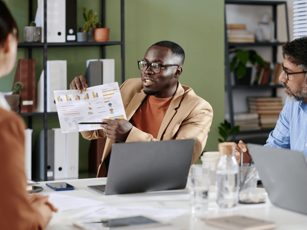 A professional presenting social impact evaluation findings to a team of three people