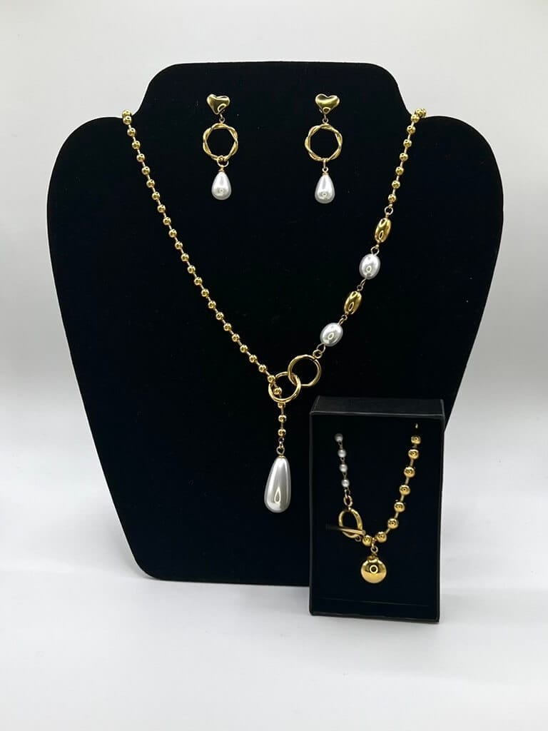 Parure de bijoux en acier inoxydable plaqué or avec perles blanches et pendentif en forme de larme : collier, boucles d'oreilles et bracelet aux détails circulaires.