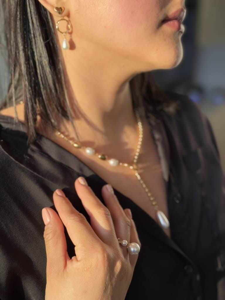 Mujer usando conjunto de joyería dorada en acero inoxidable con perlas: aretes, collar y anillo bajo luz natural