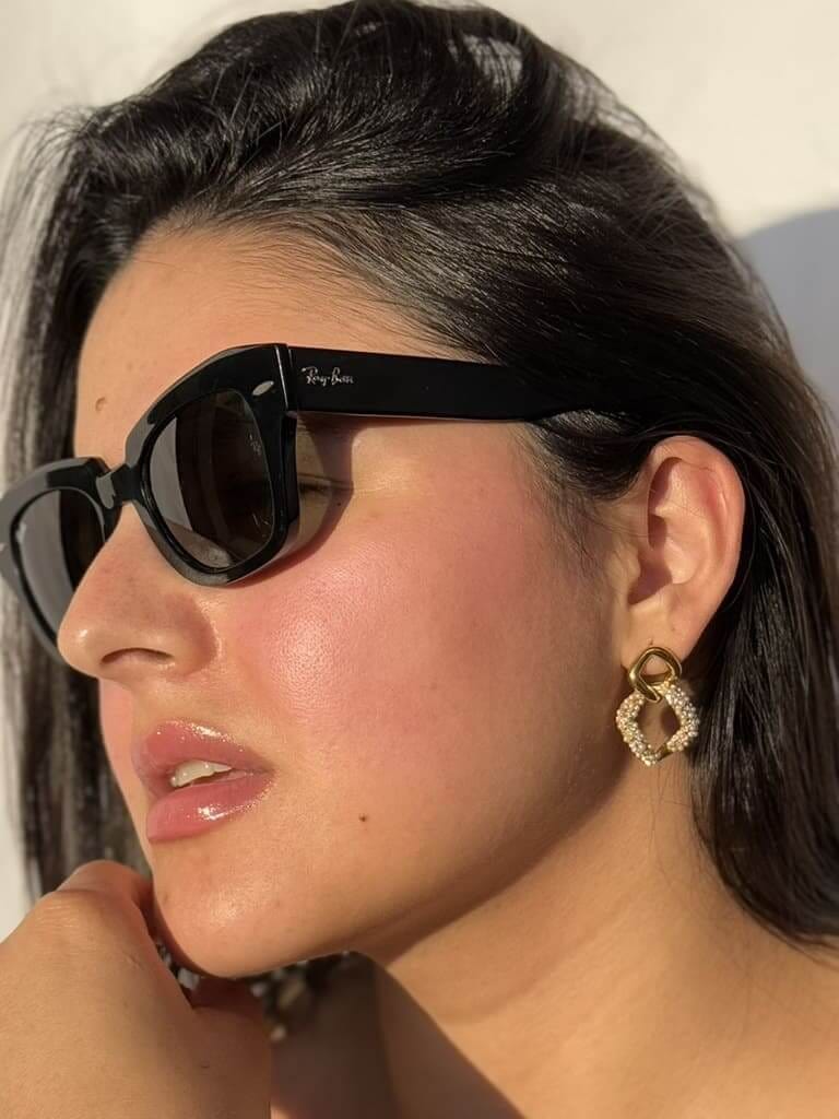 Mujer con gafas de sol luciendo aretes dorados de acero inoxidable con textura trenzada bajo luz natural