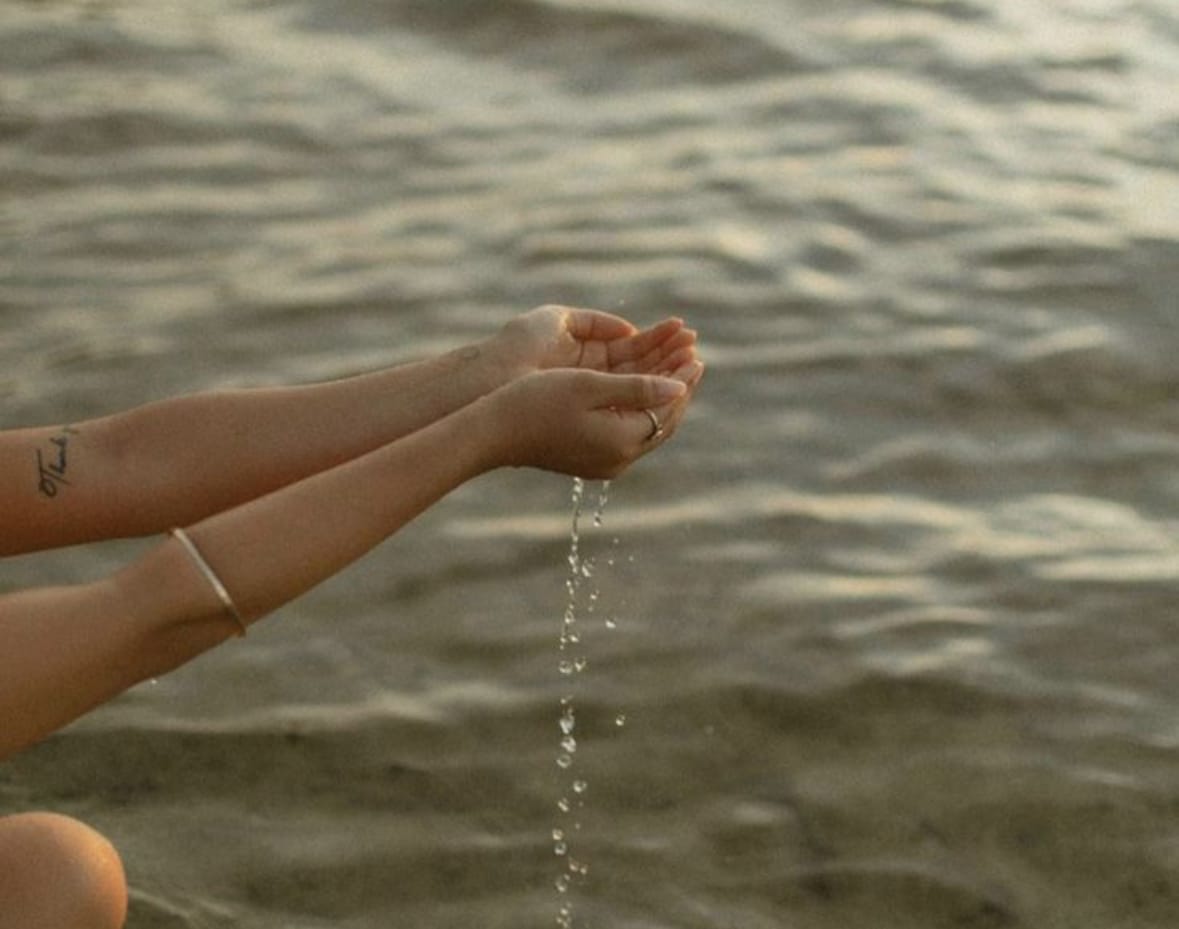 Personne au bord de l’eau effleurant la surface avec ses mains, dans un geste méditatif et apaisant