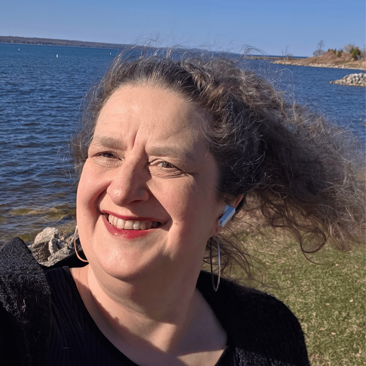 Visibility expert Andrea Stenberg stands in front of Georgian Bay with the wind blowing her long curly ponytail