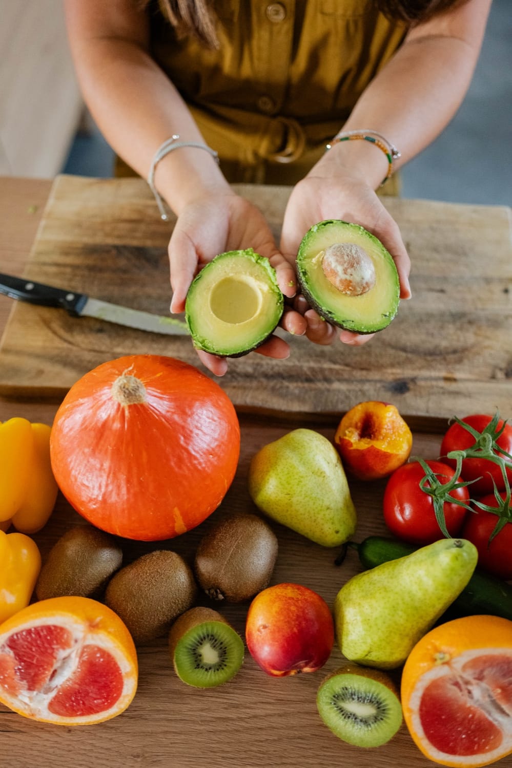 Les mains de Mélanie Padovani tiennent deux moitiés d'avocat au-dessus d'une table de fruits et légumes