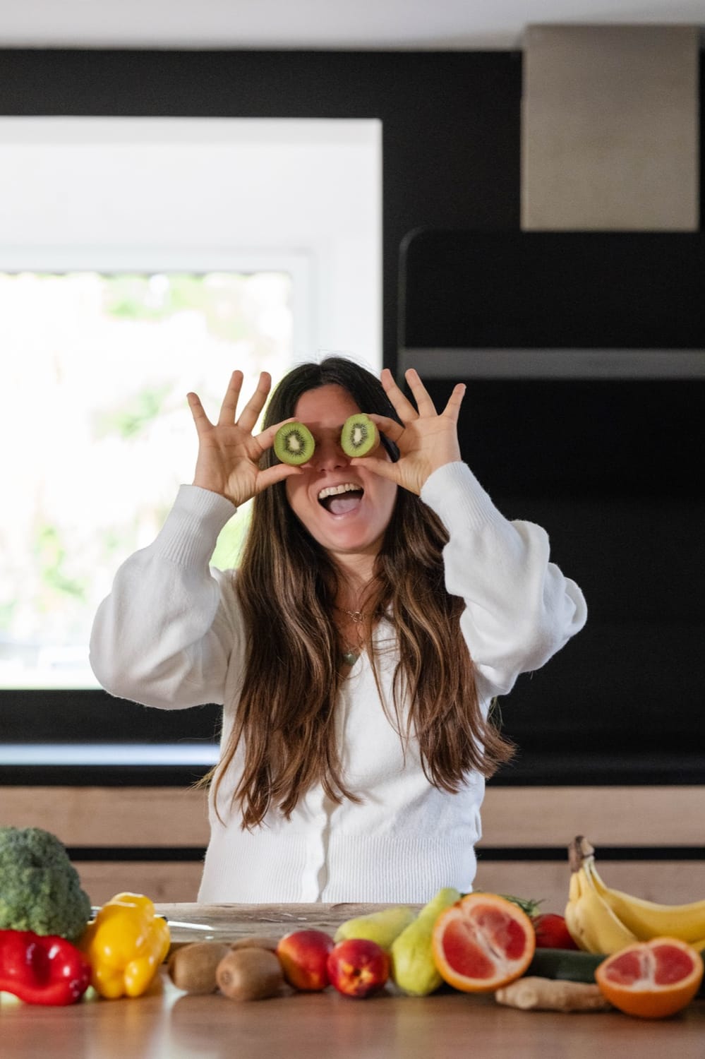 Mélanie Padovani, nutrithérapeute, rit en se cachant les yeux avec deux rondelles de kiwi dans sa cuisine