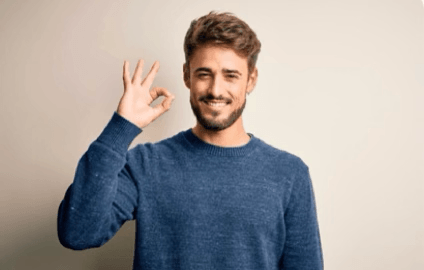 alt="Un homme souriant en pull bleu fait le signe OK de la main face à la caméra pour valider la réussite de son projet"