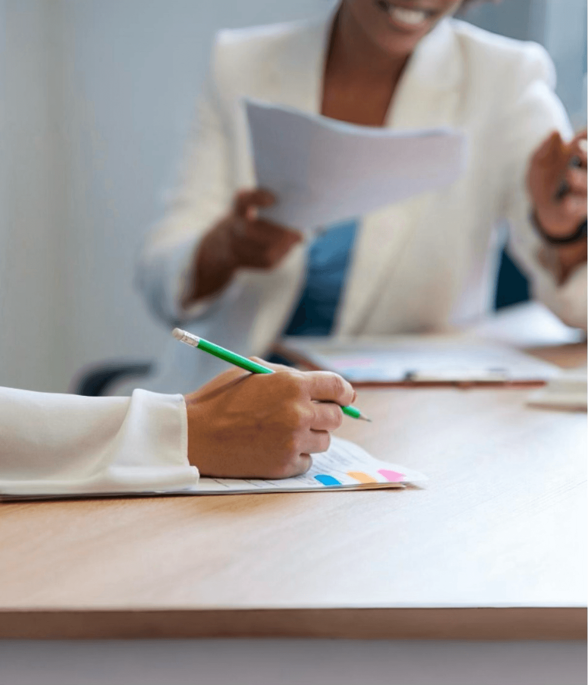 alt="Session de travail en face-à-face : gros plan sur les mains d'une personne prenant des notes et une interlocutrice souriante en arrière-plan"