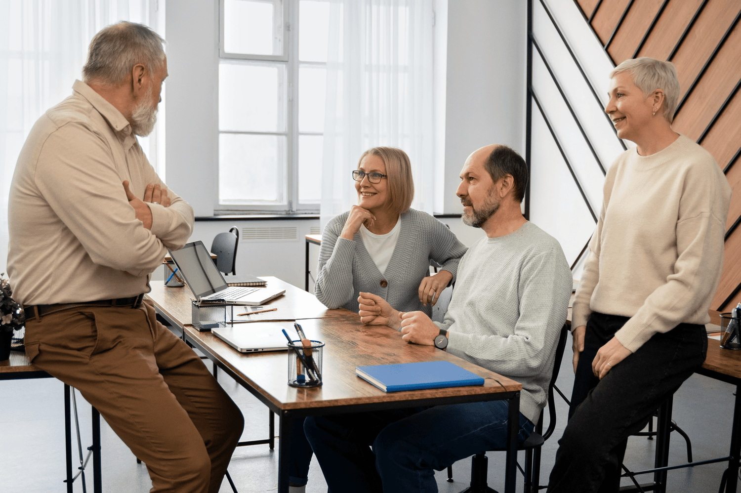 alt="Quatre entrepreneurs seniors discutant avec le sourire dans un bureau lumineux lors d'un temps d'échange convivial"