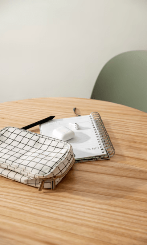 alt="Gros plan d'une trousse et d'un carnet de notes ouvert où sont posés des écouteurs, sur une table en bois avec une chaise verte"
