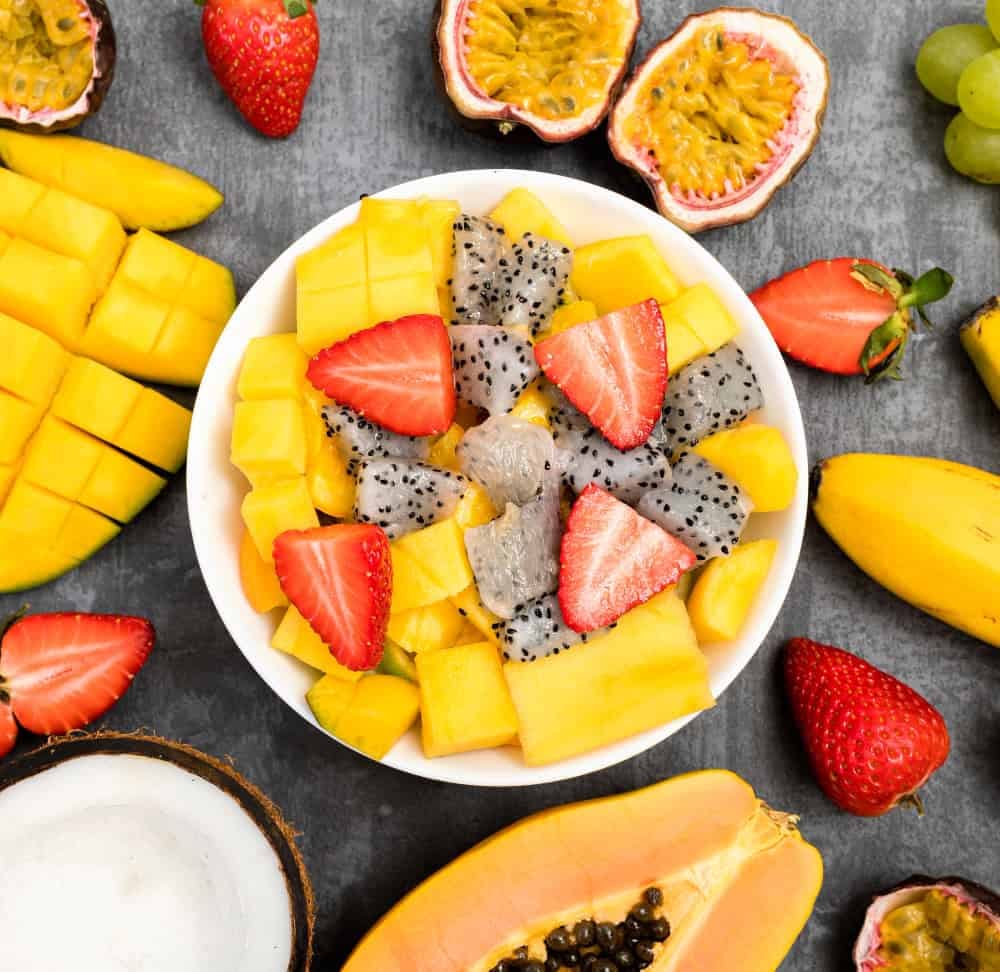 Fresh raw fruit salad bowl with mango, dragon fruit and strawberries.