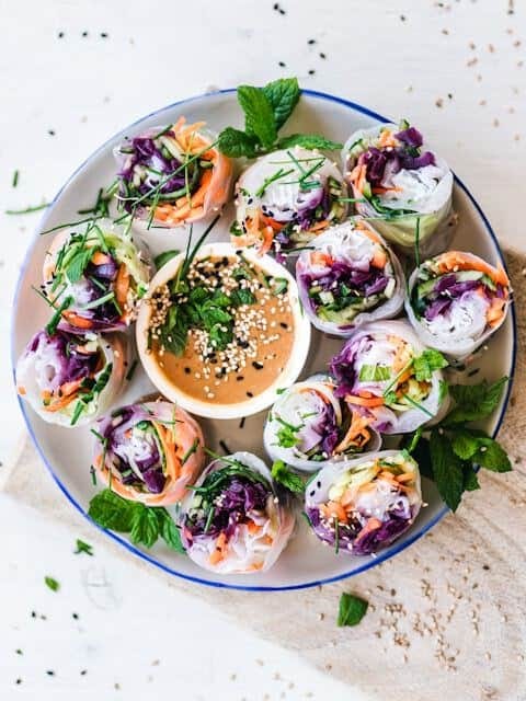 Raw vegetable rice paper spring rolls with almond dipping sauce, part of a holistic diet.