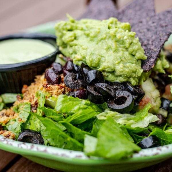 Guacamole and black olive salad bowl with dehydrated seed cracker chips