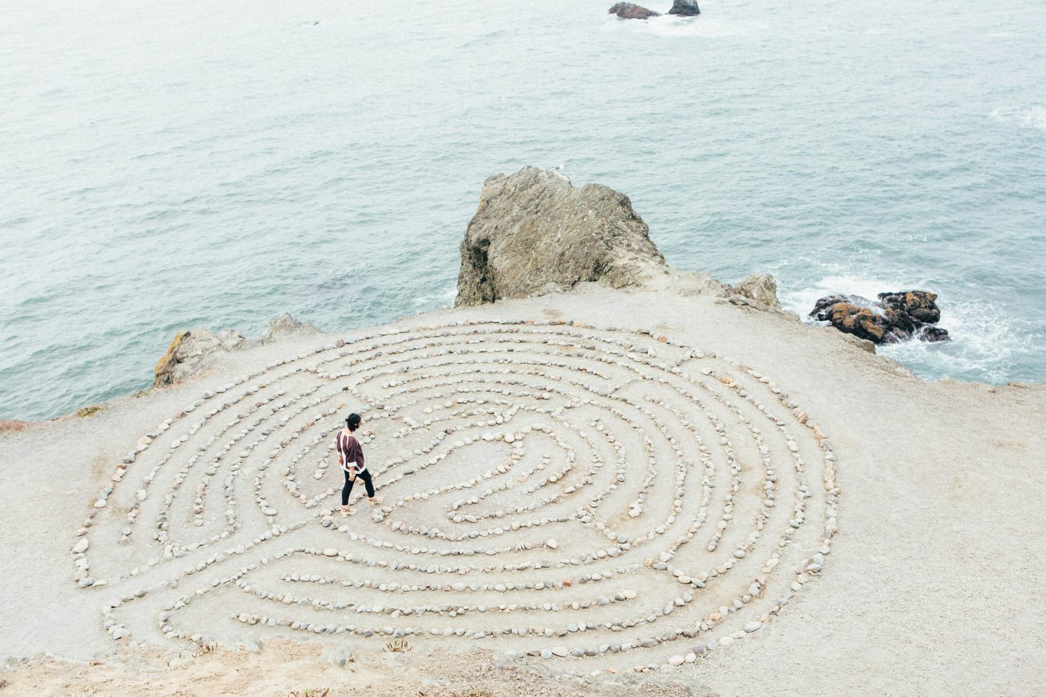 Image of a person walking on a beach within a labyrinth made of rocks on the beach