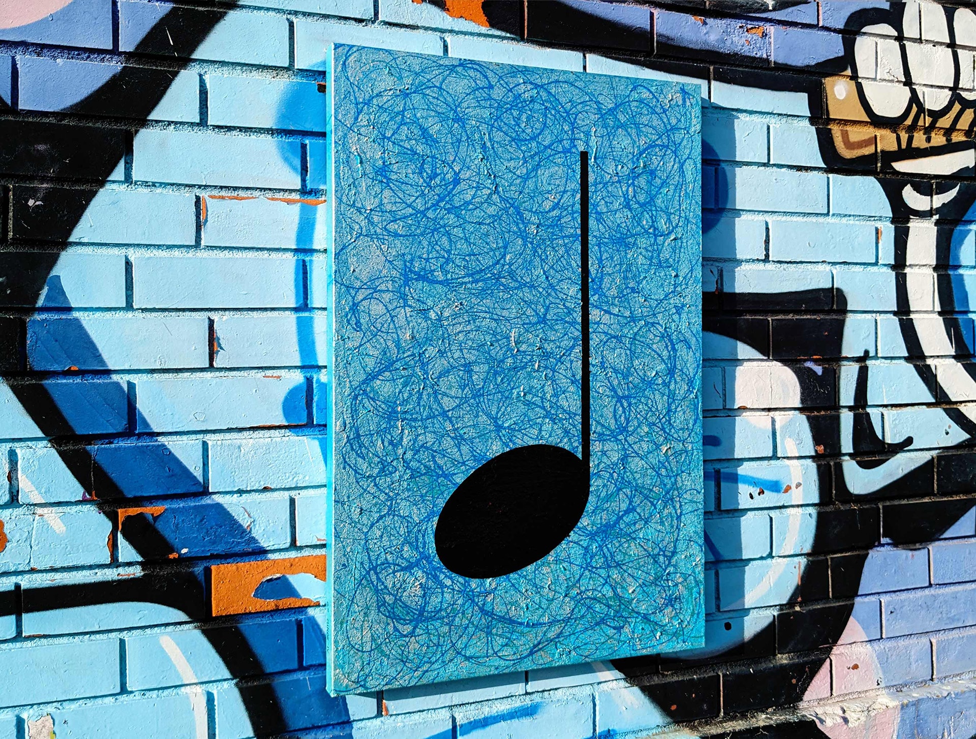 Black mannequin wearing sunglasses and headphones standing in front of a gallery wall with four multiple size framed art prints