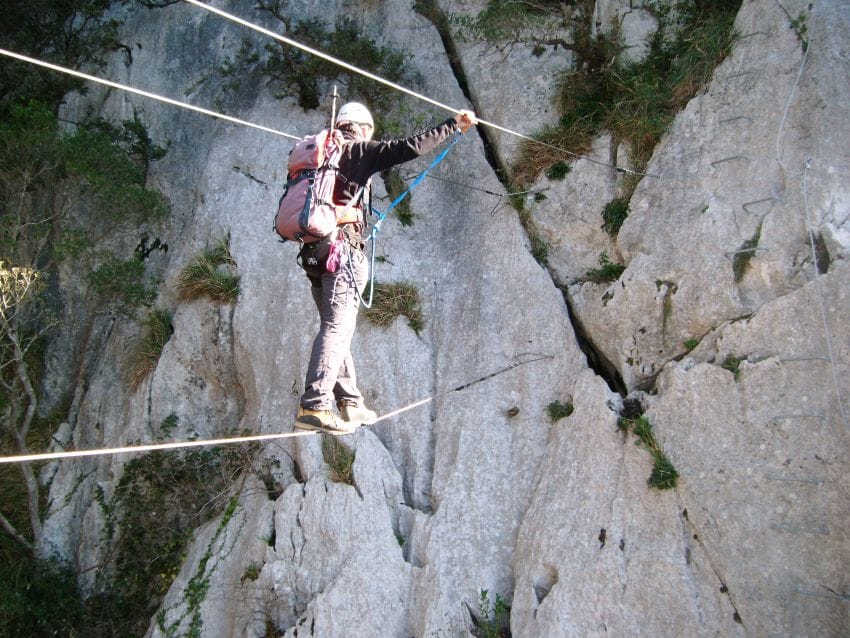 Persona cruzando un puente tibetano en una vía ferrata, concentrada en el equilibrio y la seguridad para ilustrar que el silencio mental no es dejar la mente en blanco, sino tener un enfoque único.