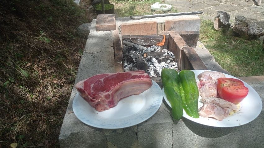 Plato con chuletón de ternera a la brasa, pimiento y tomate junto a una barbacoa encendida, representando la cena ideal frente a la realidad de una nevera medio vacía.
