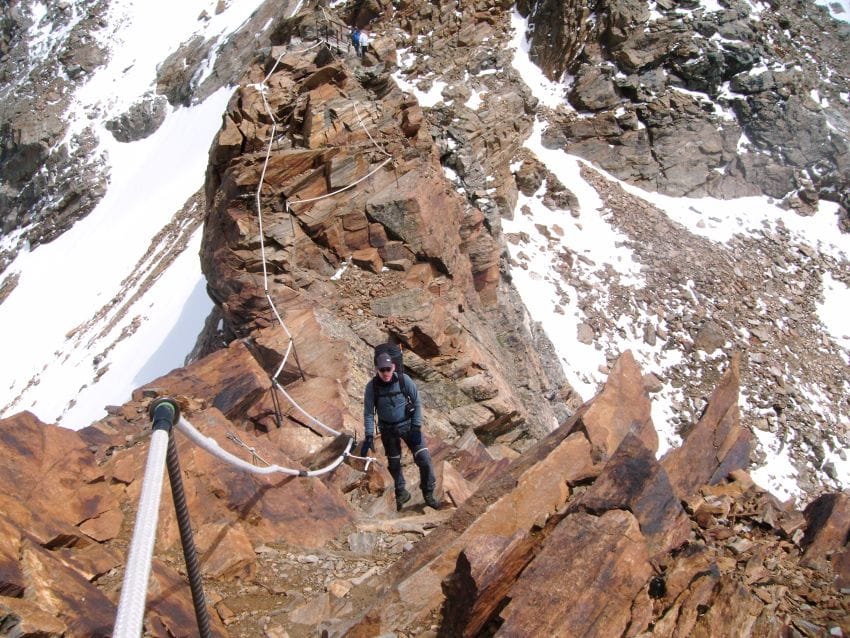 Montañero avanzando por una cresta de alta montaña con maromas guía, ilustrando el camino directo y la claridad frente al exceso de análisis.