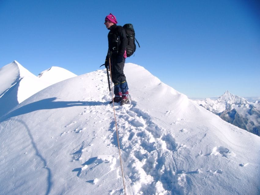 Montañero haciendo una pausa de pie en una arista de nieve contemplando el paisaje, representando el descanso real del cerebro frente a la distracción.