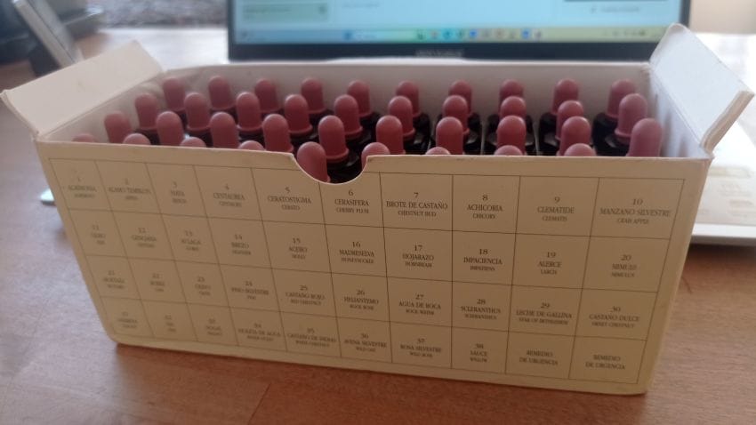 Caja organizadora con stock de frascos de Flores de Bach sobre una mesa de consulta con un ordenador al fondo.