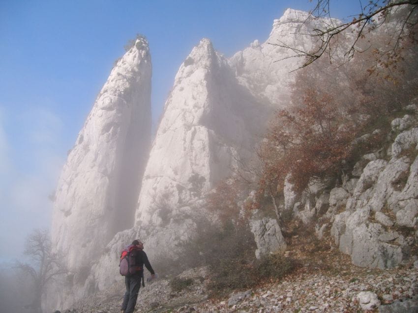 Montañero con mochila observando una gran pared de roca envuelta en niebla durante una caminata