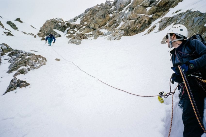 Escalador en reposo asegurando a su compañero en la nieve como metáfora de calma y seguridad del cuerpo