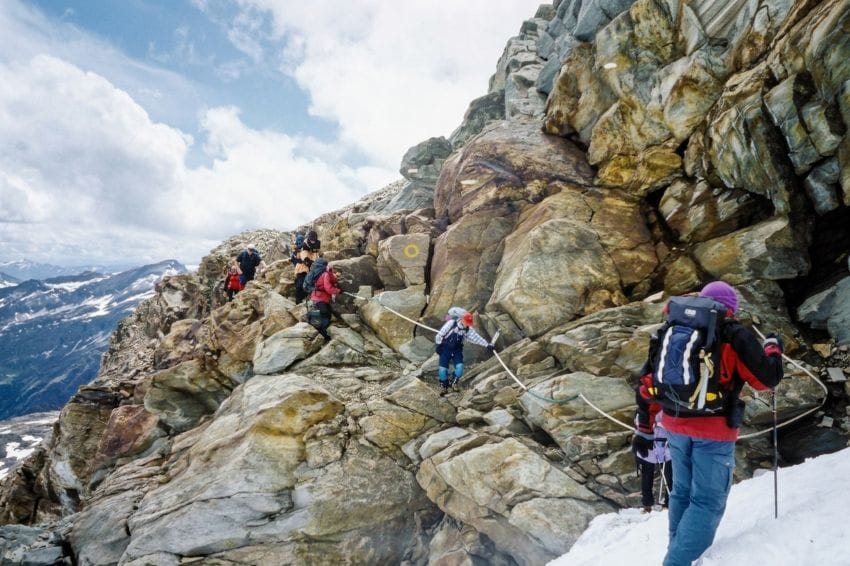 Senderistas en un paso de montaña difícil agarrados a una cuerda de seguridad, metáfora visual de la tensión física necesaria versus la necesidad de soltar la guardia para gestionar el estrés.