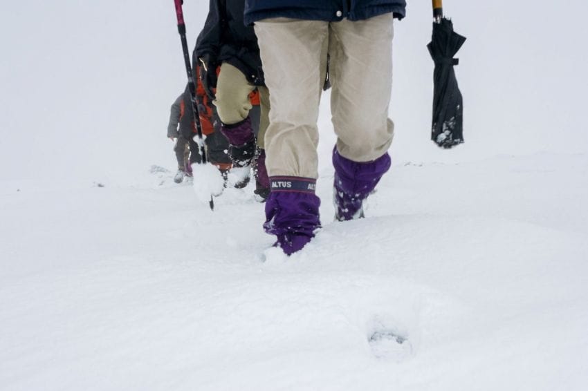 Primer plano de piernas de montañeros con polainas Altus hundiéndose mecánicamente en una extensión de nieve blanca y monótona, representando el avance en piloto automático en la naturaleza.