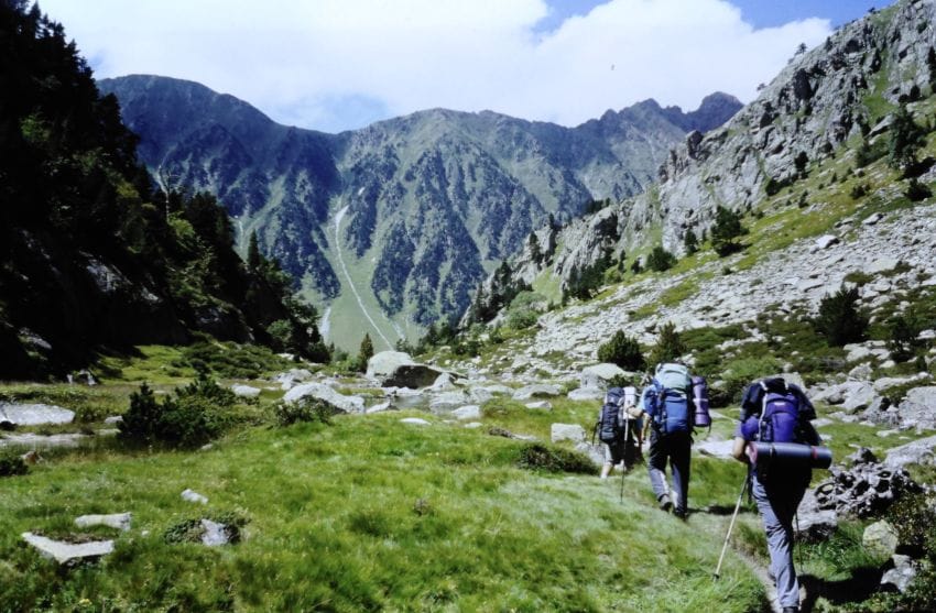 Montañeros caminando de espaldas con mochilas pesadas representando la acumulación de carga mental y sobrecarga emocional.