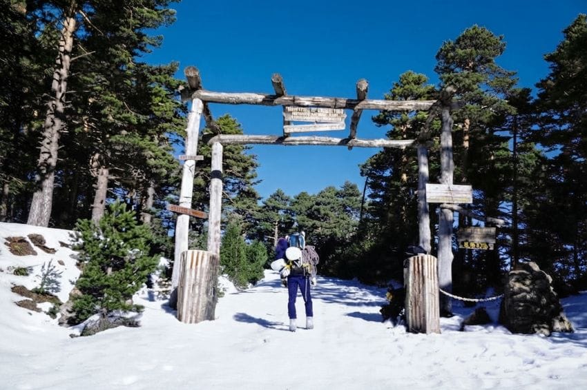 Montañero cargando equipo pesado y cuerdas bajo la nieve, representando el desgaste diario y el esfuerzo constante.