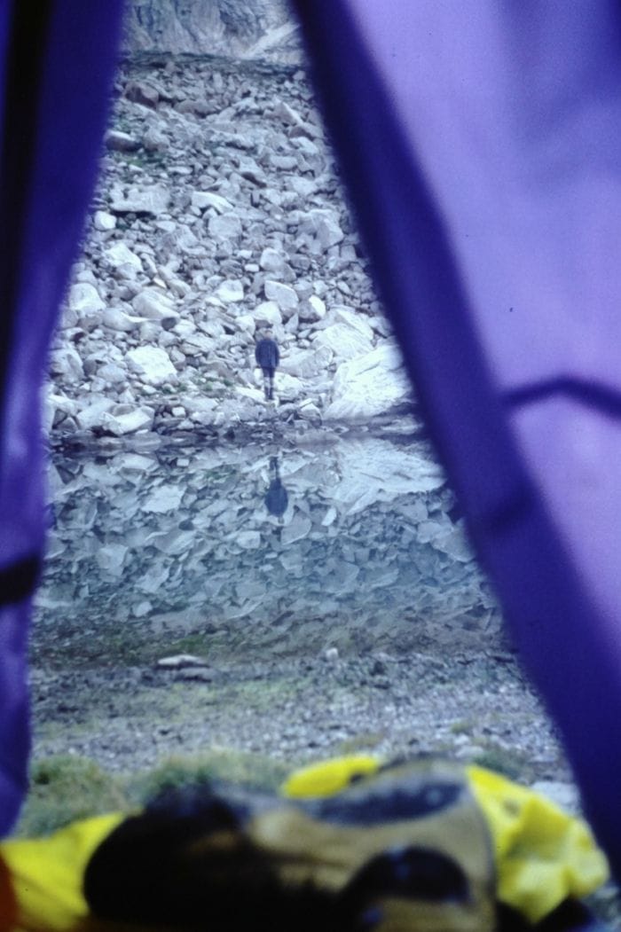 Vista desde el interior de una tienda de campaña hacia un lago de montaña, representando una pausa estratégica y descanso consciente para recuperar la perspectiva y no agotarse en el camino.