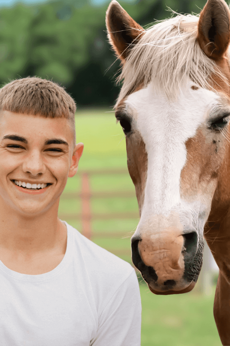 Smiling teen boy standing next to a horse in a calm pasture during a Spirited Hooves equine-guided confidence session